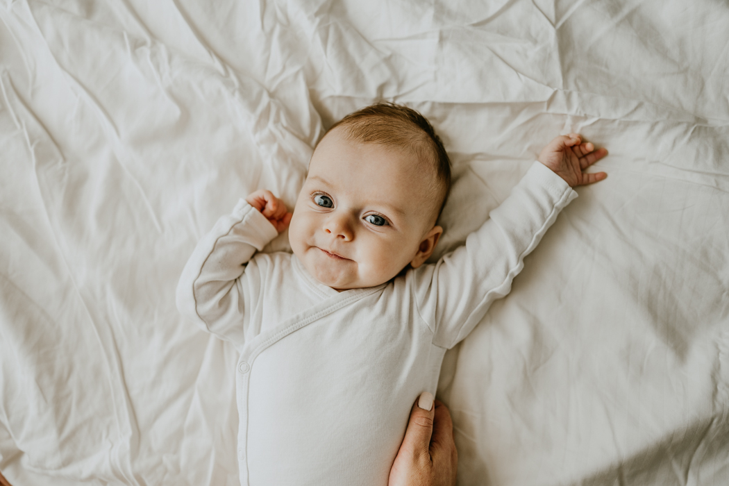 fotografia słodkiego niemowlęcia leżącego na białej pościeli podczas domowej sesji noworodkowej